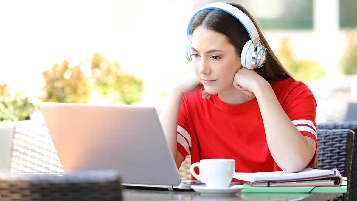 A woman wearing headphones looks at a laptop