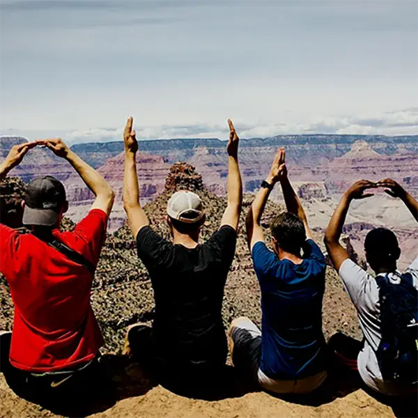 Four students sitting over a valley making the O-H-I-O