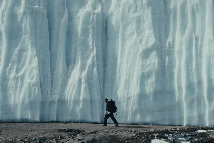 man walking beside a huge white glacier with a backpack