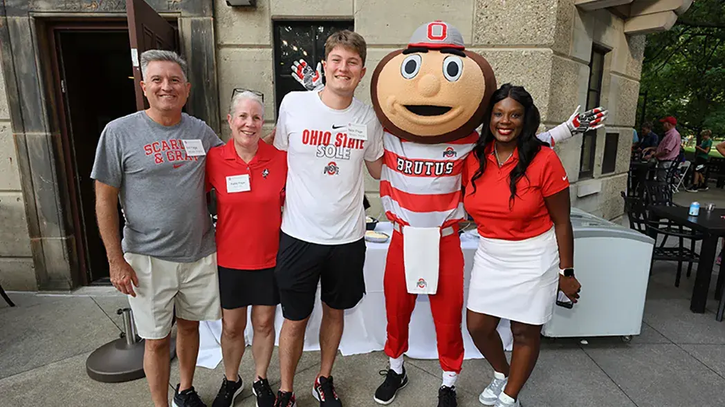 An Ohio State student poses for a picture with his parents, Brutus Buckey and a parent's advancement council member