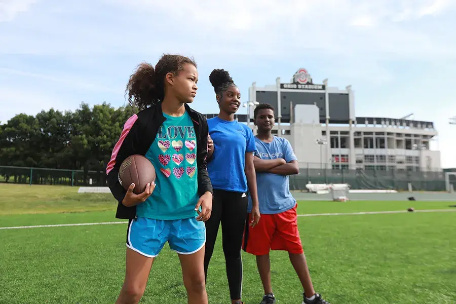 Three kids stand outside in front of Ohio Stadium