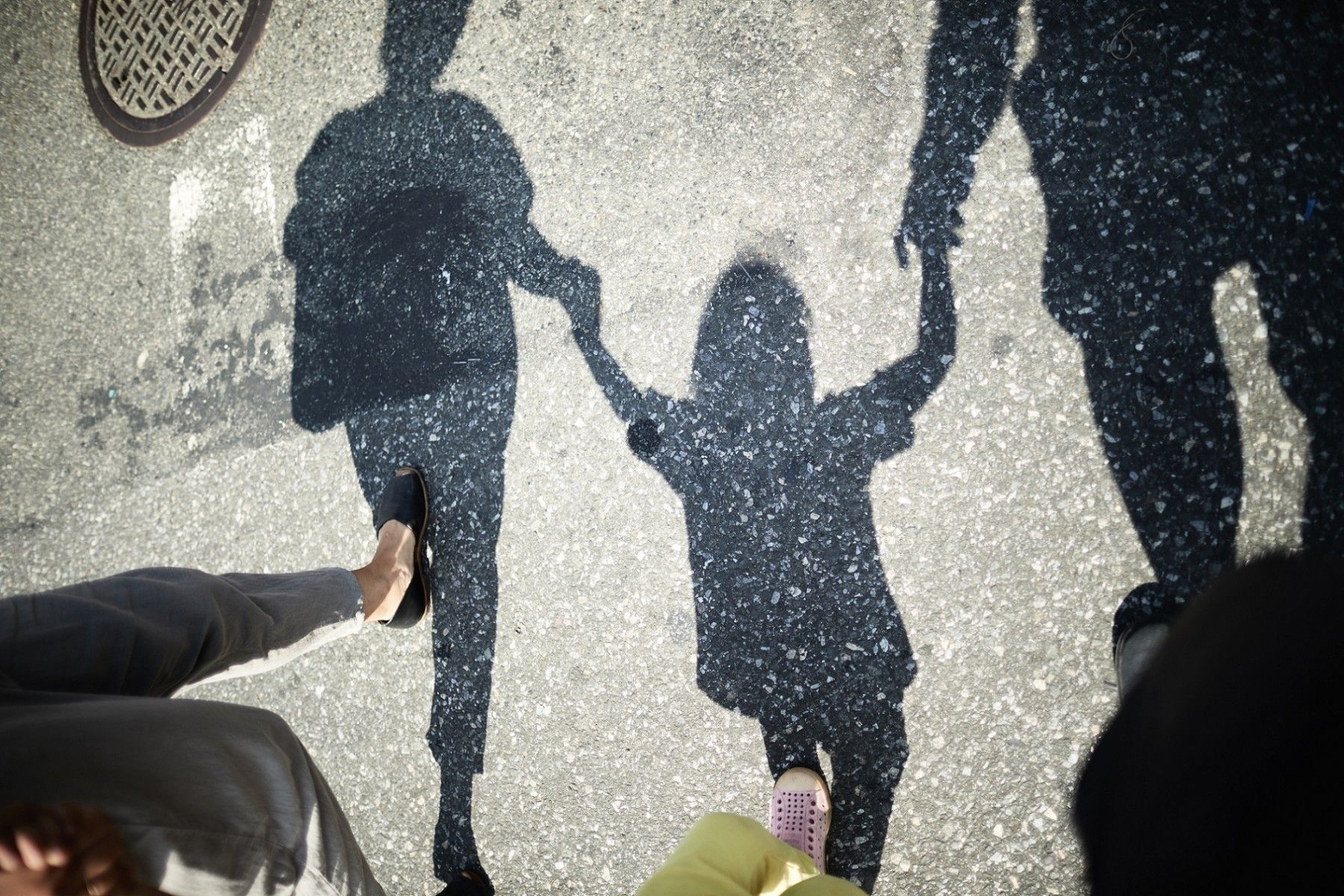 Shadows on pavement reveal a young child holding hands with two adults.
