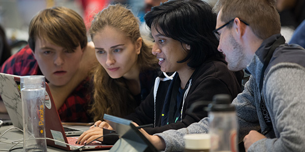 a team of students work together around a laptop