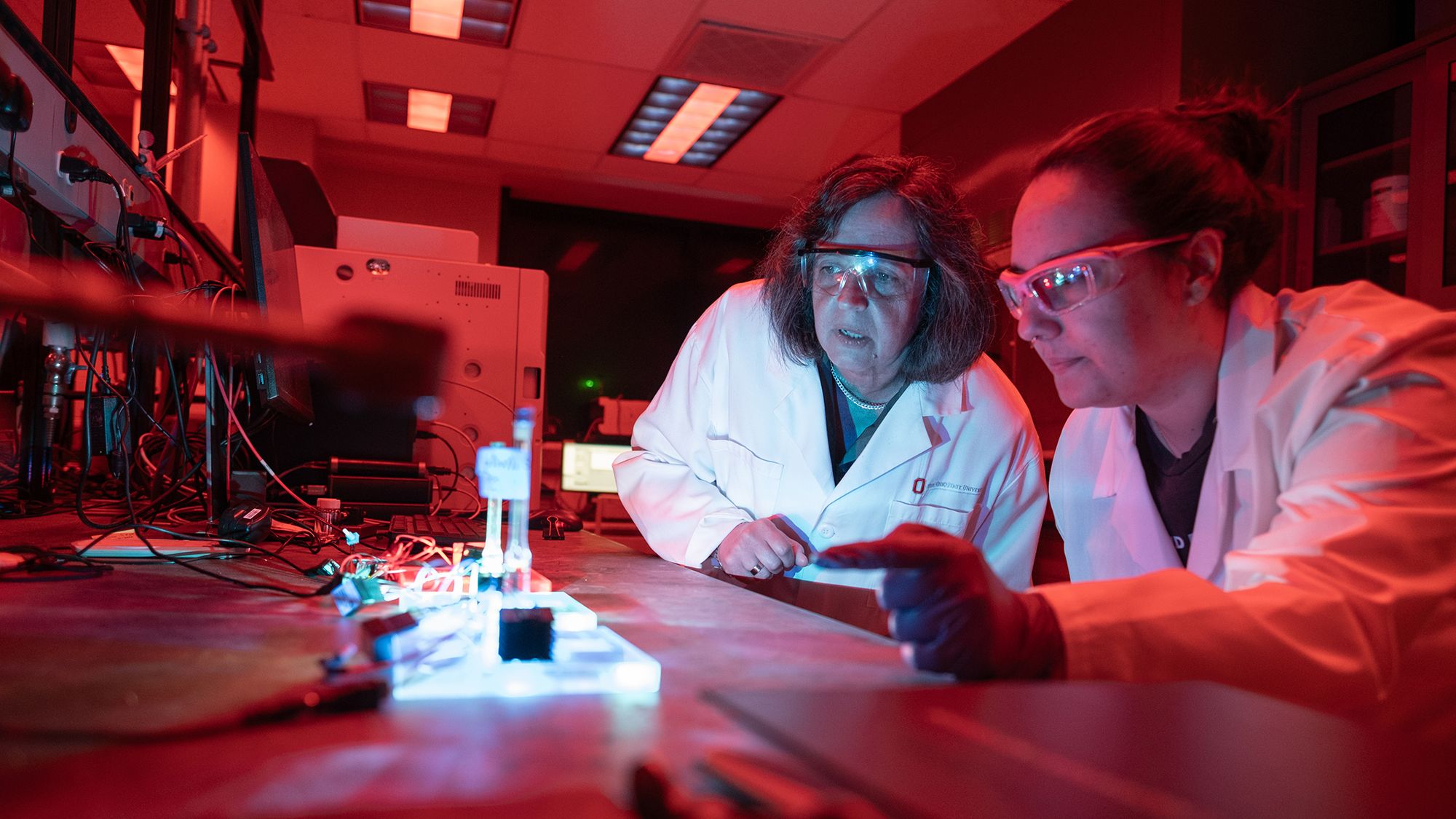 Claudia Turro examines a light experiment while flanked by a student