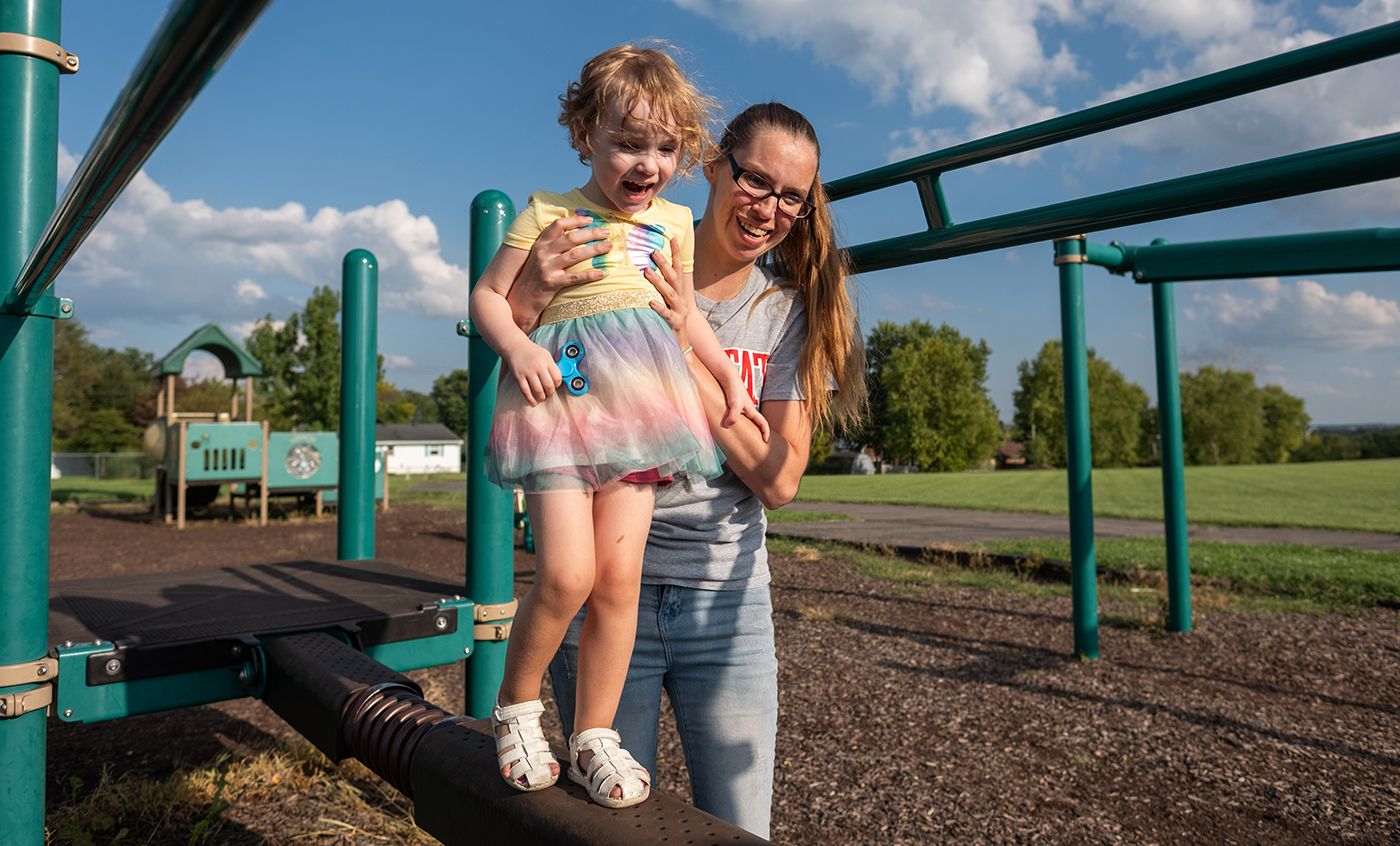 A mother holds her daughter as she walks across a balance beam on a playground