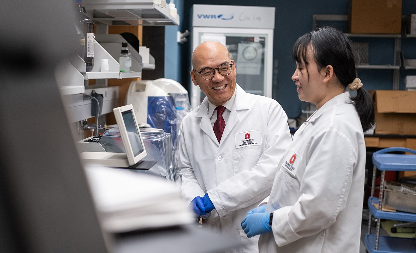 A researcher in a white lab coat talks with a colleague