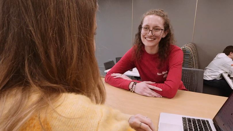 A woman sitting at a desk smiles at a woman sitting across from her