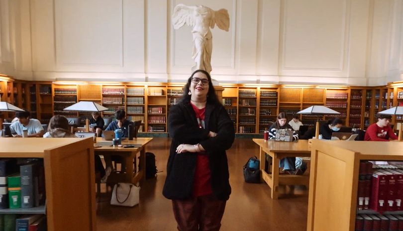 A young woman stands with her arms folded in the grand reading room of Ohio State's Thompson Library