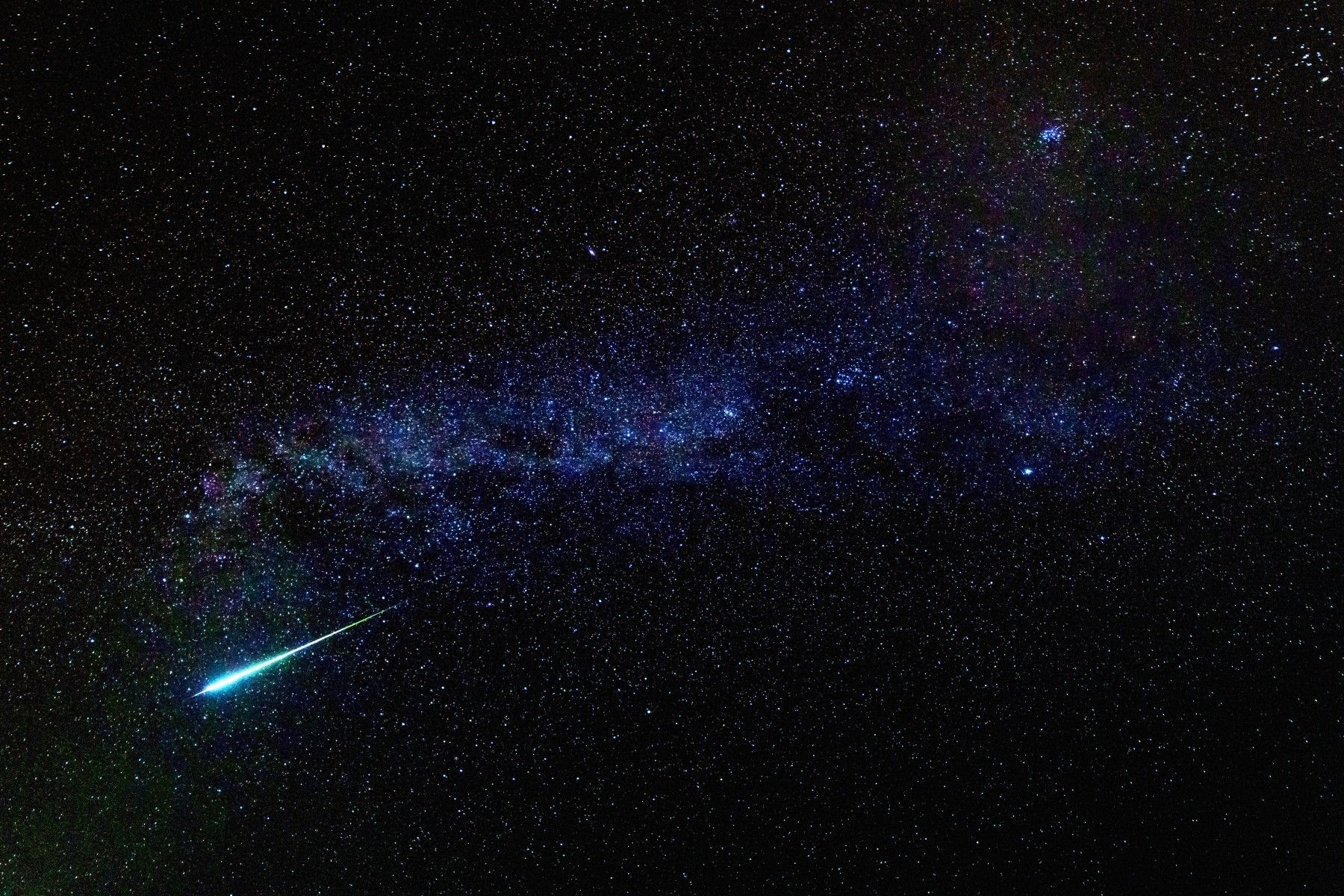Bright blue meteor flying through a dark starry sky
