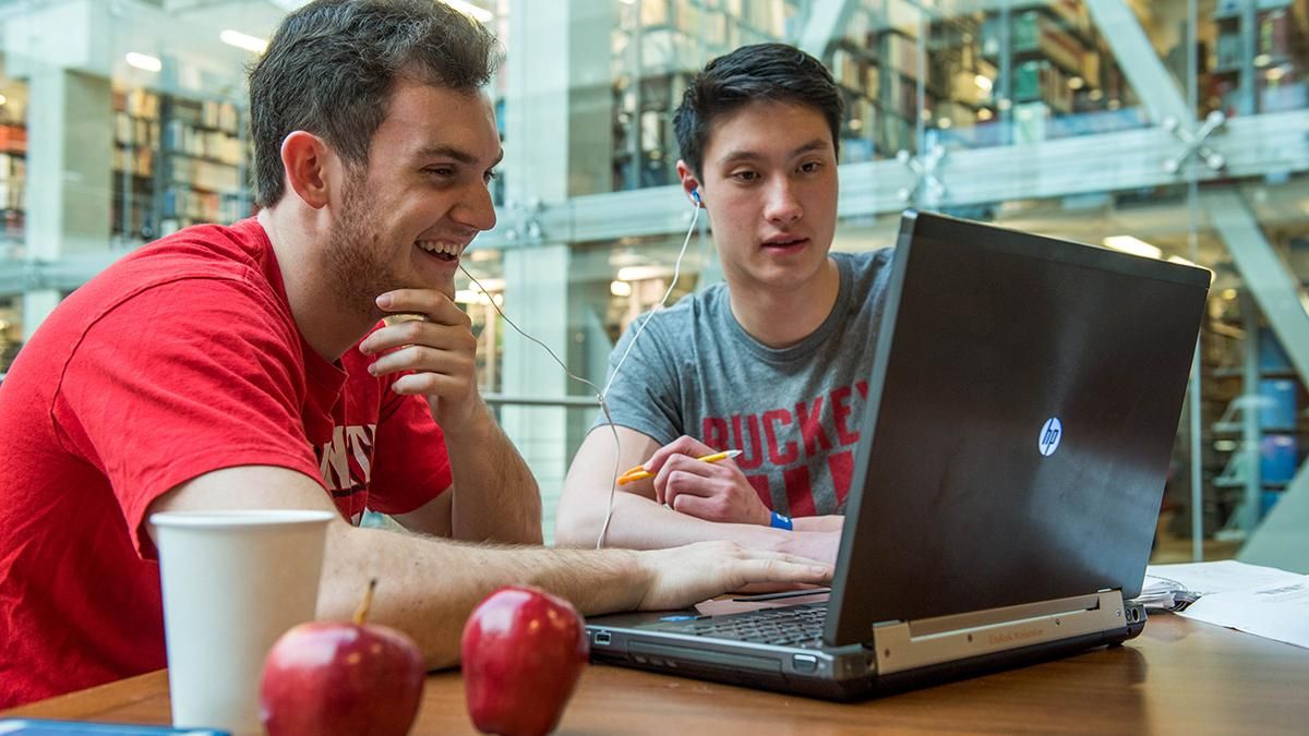 Two male students sit next to each other and look at a laptop while sitting in the Thompson Library