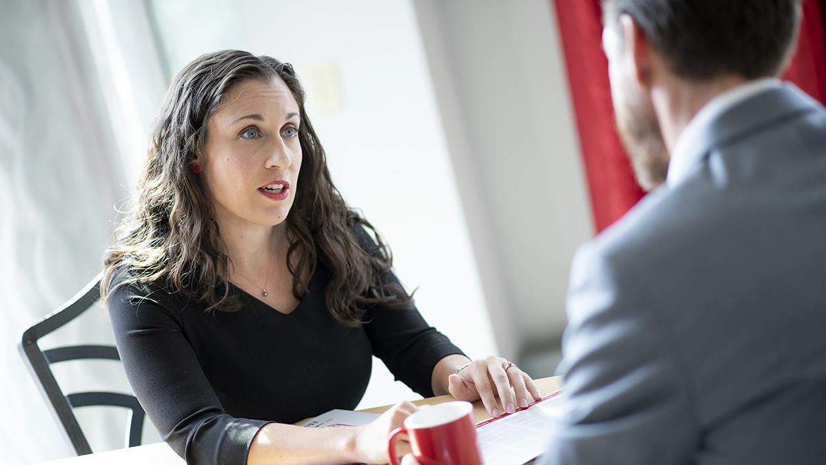 A woman interviews a man holding a red coffee mug