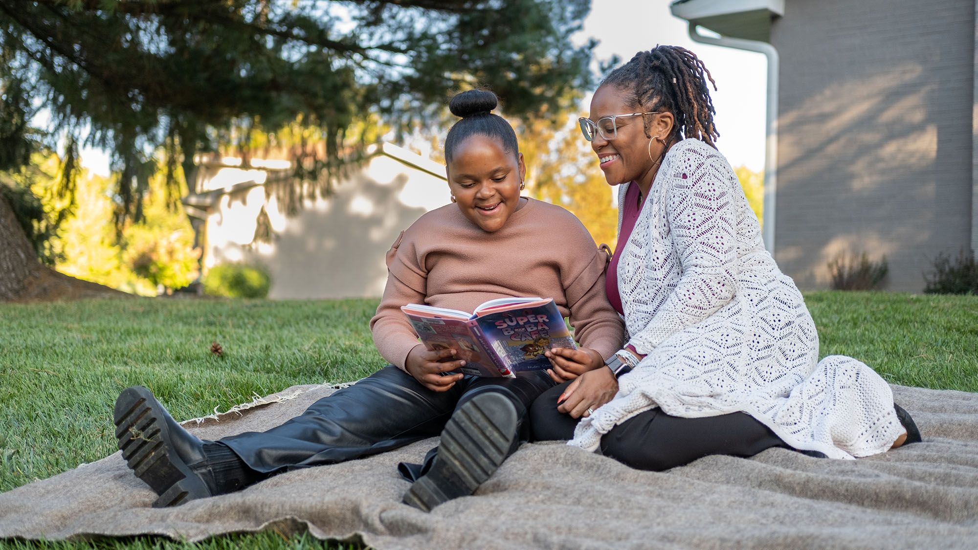 A mother and her daughter sit on a lawn and read together.
