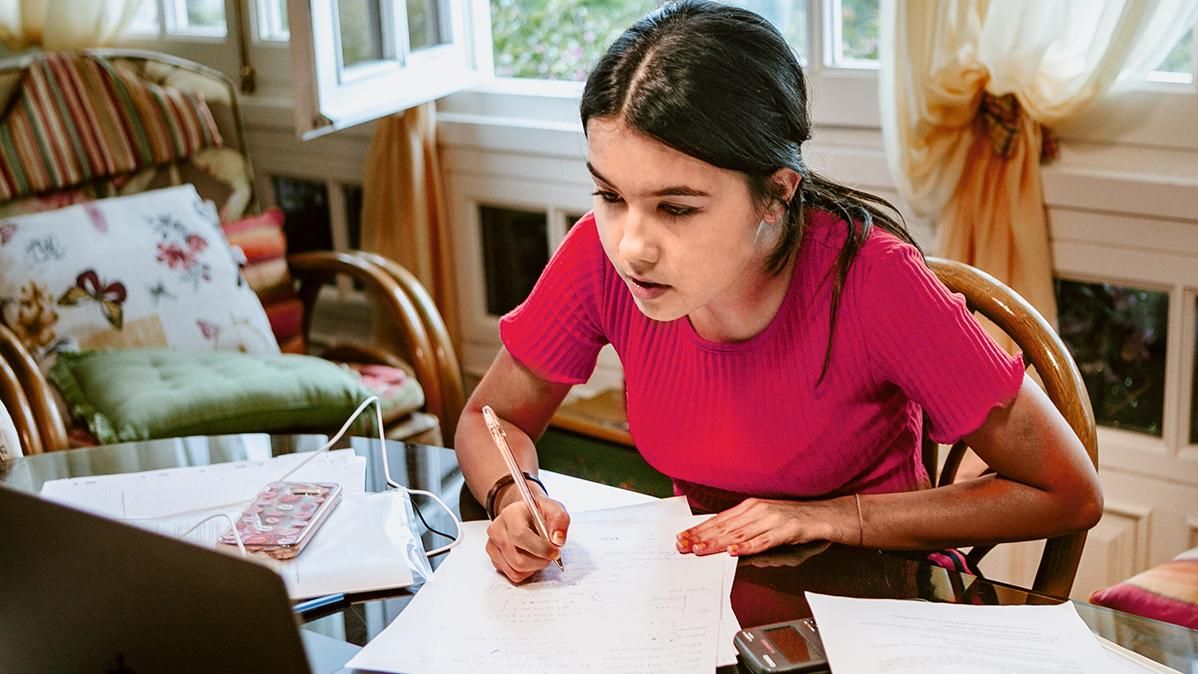 A student looks at a laptop and writes on paper while sitting at home