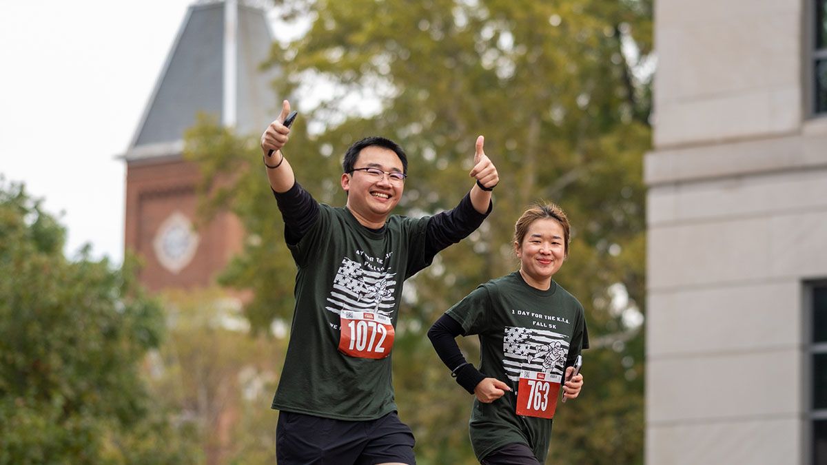 A student gives the thumbs up while running past University Hall in the One Day for the KIA 5K