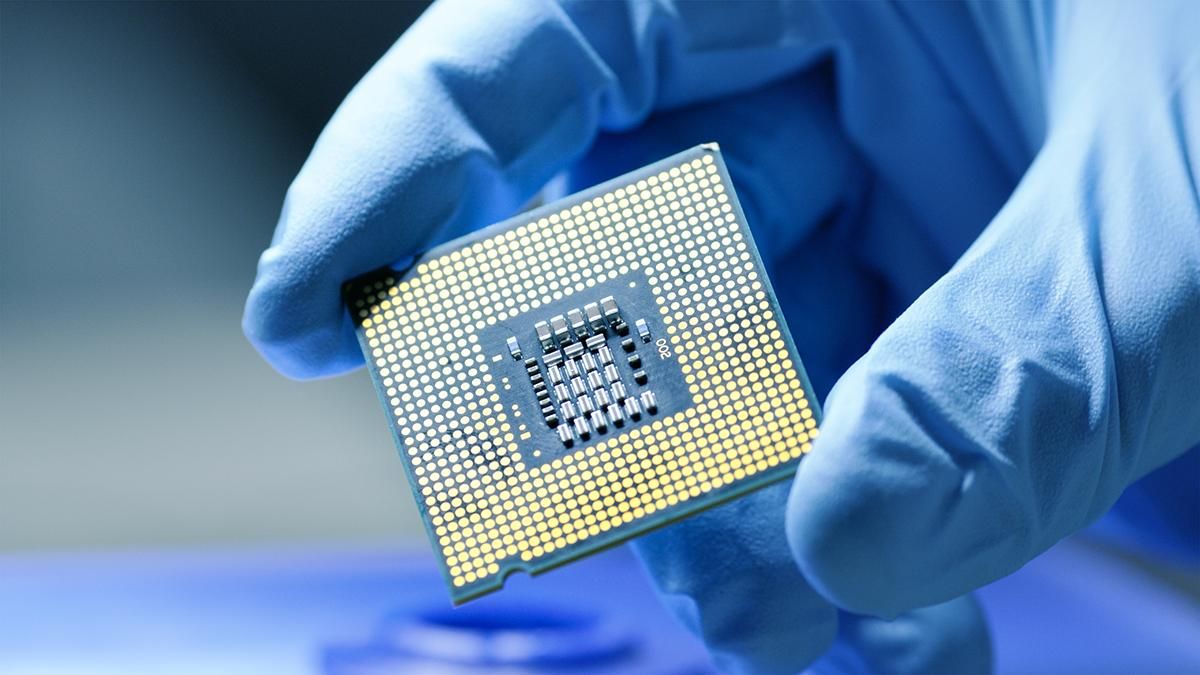 A blue-gloved hands holds a microelectronic chip