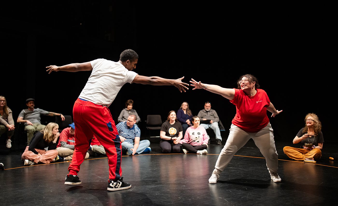 Two participants touch hands on stage as individuals watch during a performance that is part of the Shakespeare and Autism program at Ohio State