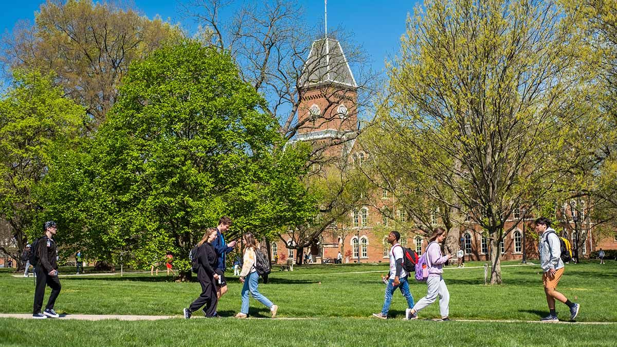 Students walking across the Oval. In the background is an academic building surrounded by trees.