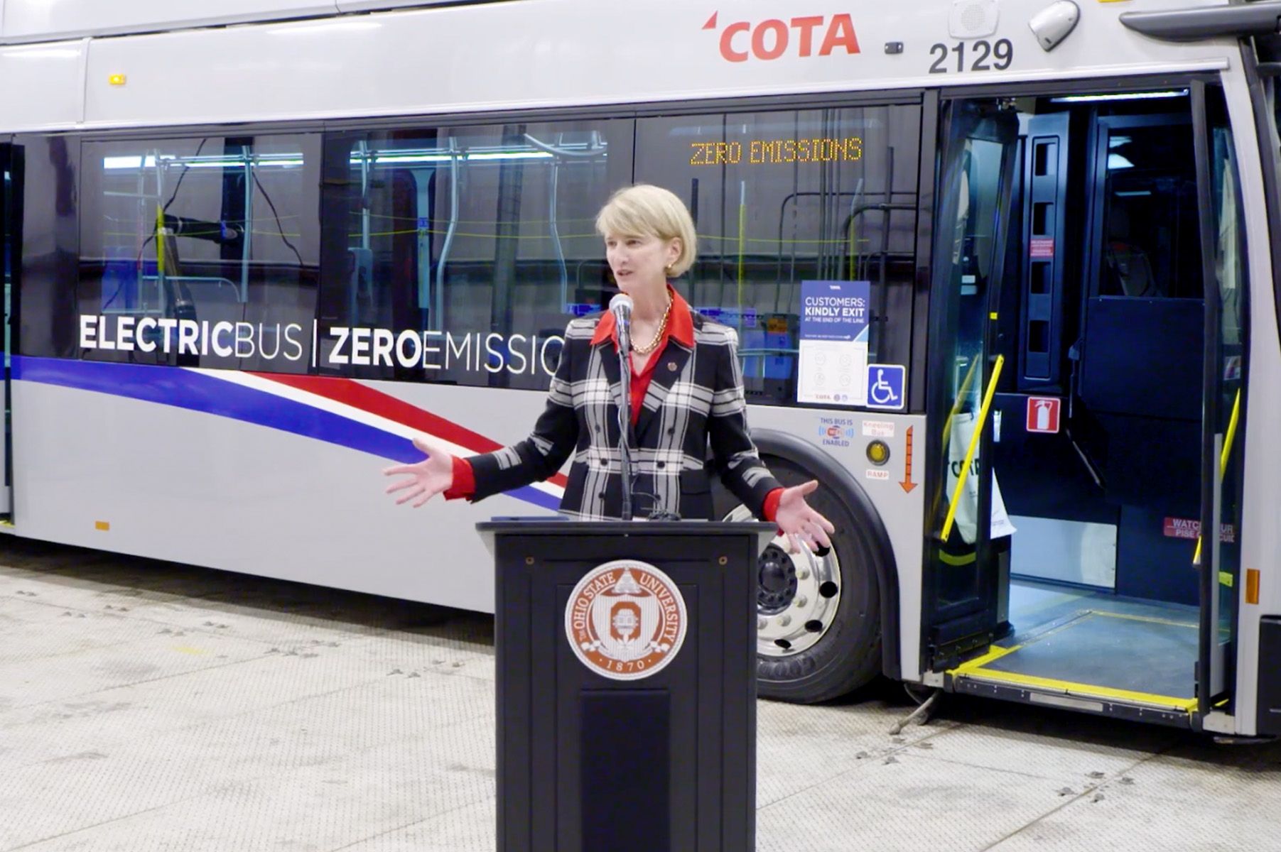 Woman at podium speaking in front of zero emission bus