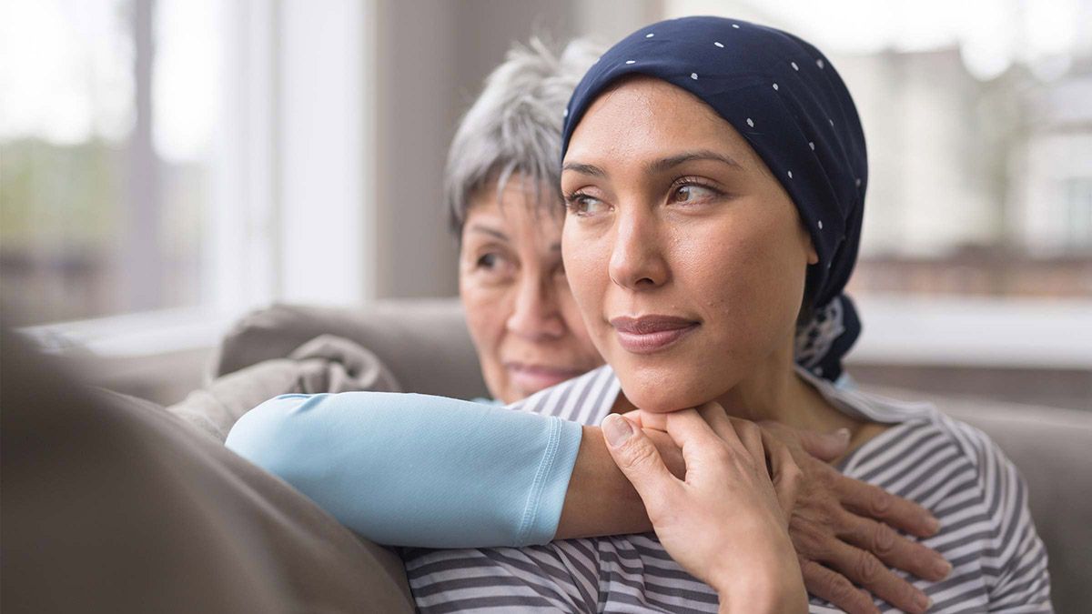 Woman wearing a headscarf looking out a window with an elderly woman