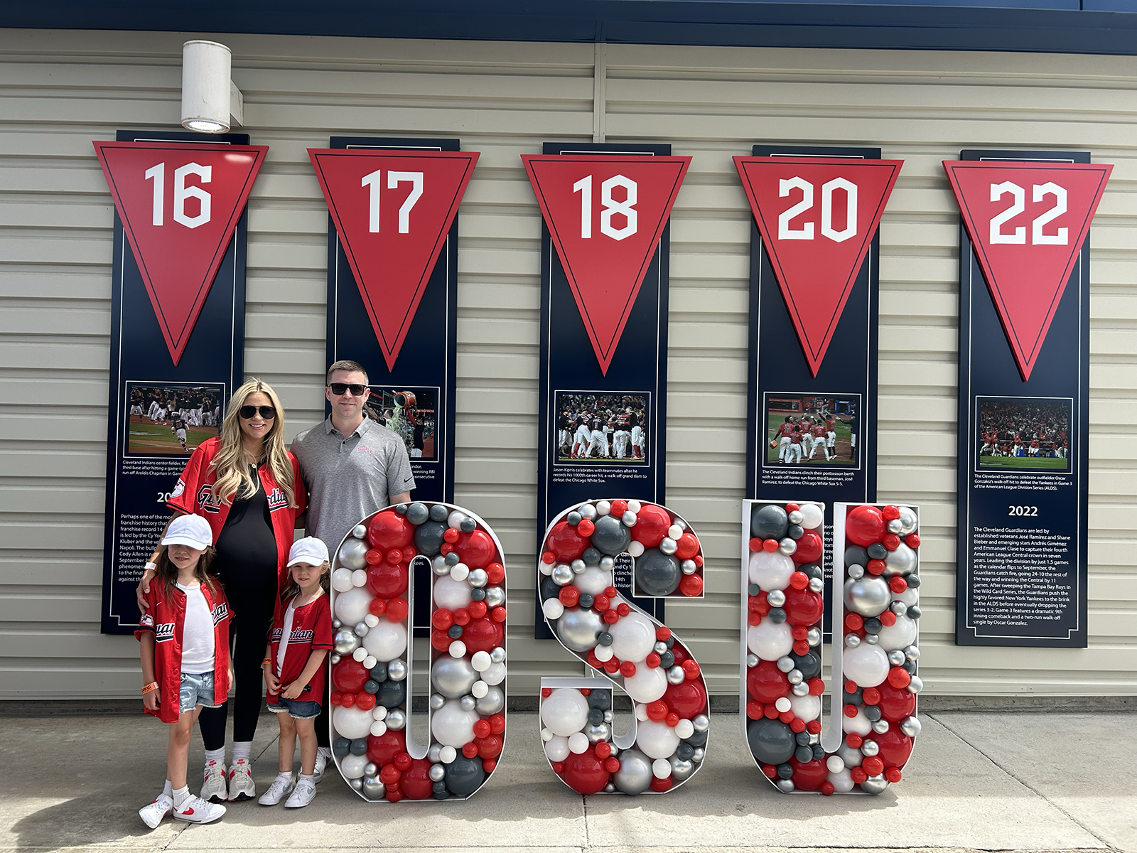 two adults and two kids stand next to balloons that spell out osu