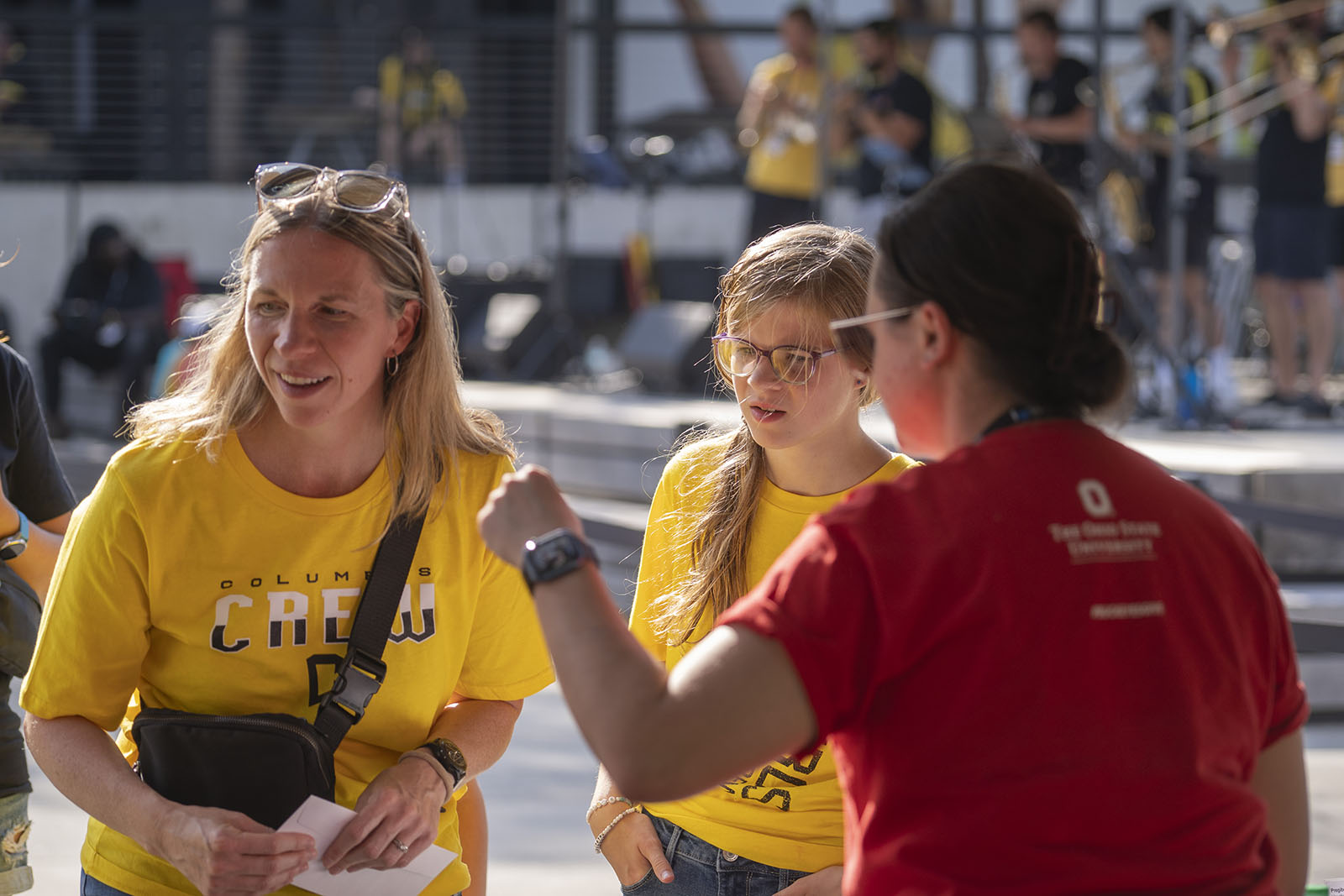 An Ohio State staff member giving verbal guidance to two fans wearing Columbus Crew T-shirts