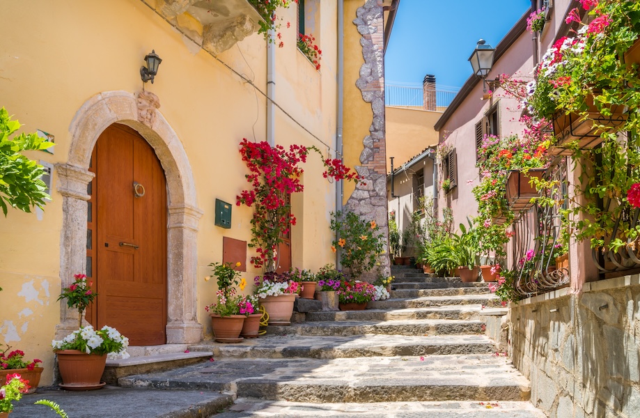 a narrow pathway with flower-clad buildings lining each side