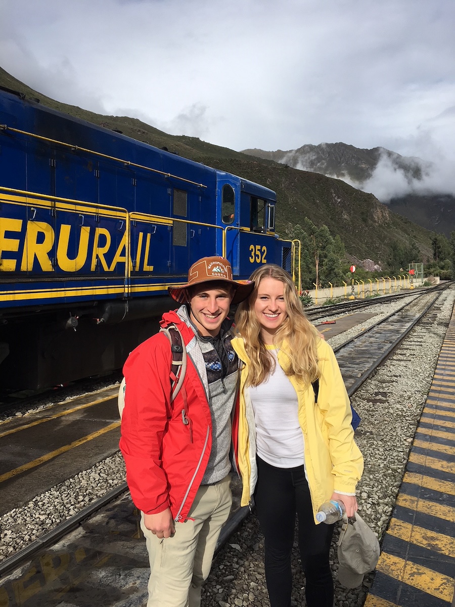 Two travelers at the rail station with a train in the background