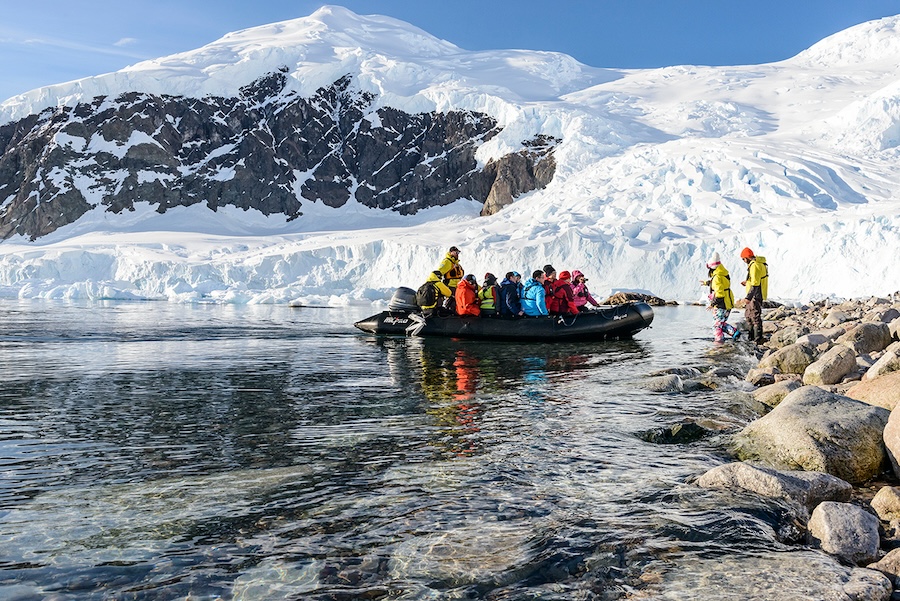 A group of travelers in a zodiac skiff landing on the shore