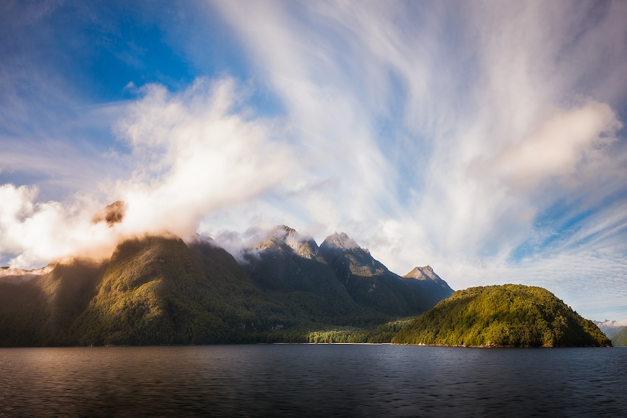 Clouds above mountains and the ocean with a bright blue sky