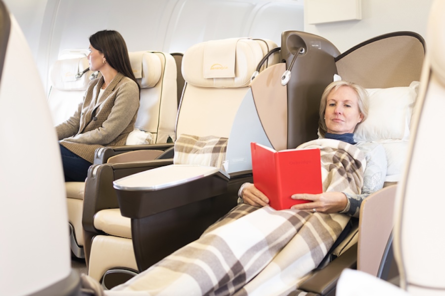 two people traveling in the private jet. One laying down reading a book and one sitting up looking out the window