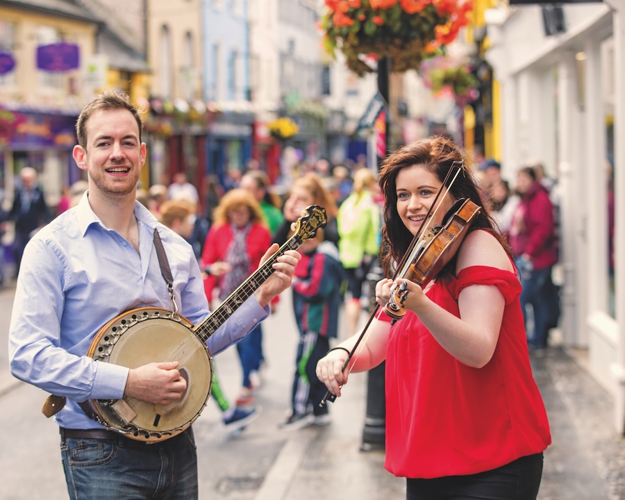 Two musicians playing instruments on a busy street sidewalk
