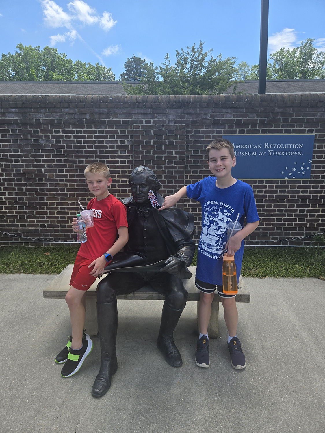 Two boys on a bench with a statue of George Washington, in front of the American Revolution Museum at Yorktown, Virginia.