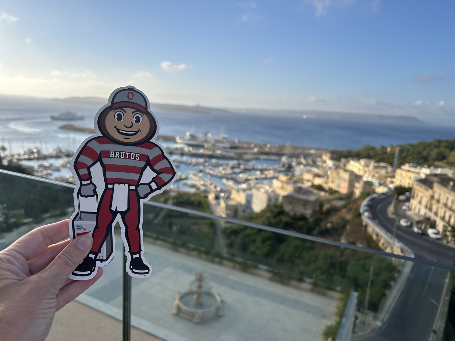 Brutus on a balcony overlooking a small town and a bay with blue water in Ghanjnsielem, Malta.