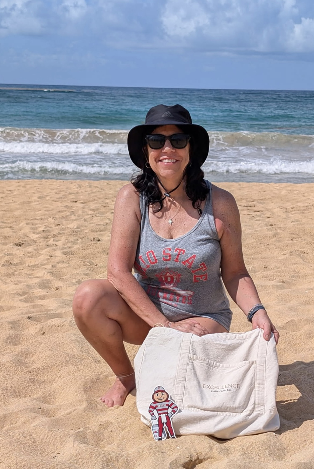 Brutus on a white beach with a woman kneeling, wearing an Ohio State tank top and blue ocean behind her in Punta Cana, Mexico.