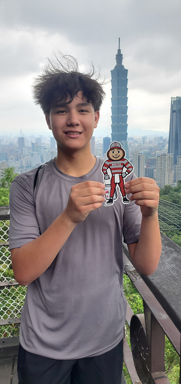 Brutus being held by a young man on a balcony in front of the Taipei 101 building in Taiwan.