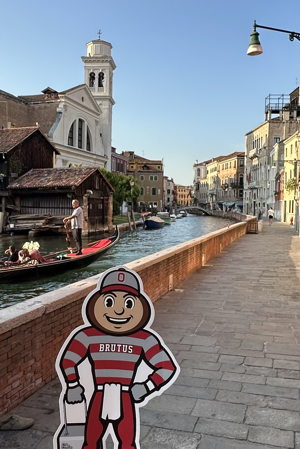 Brutus on a sidewalk in front of a gondola on a narrow canal in Venice, Italy.