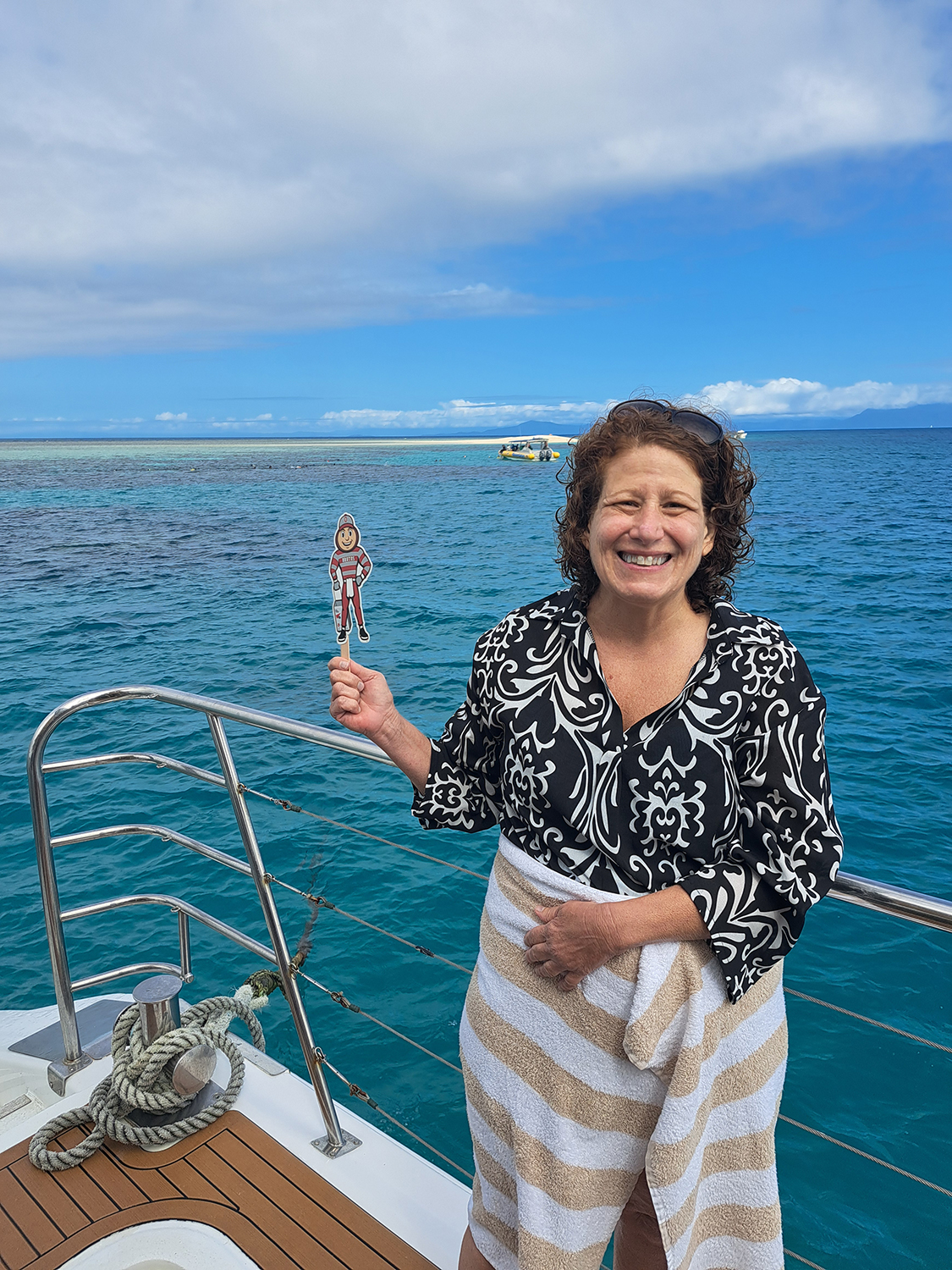 A woman on a boat, holding Brutus, with crystal blue ocean water in the background in Port Douglas, Australia.