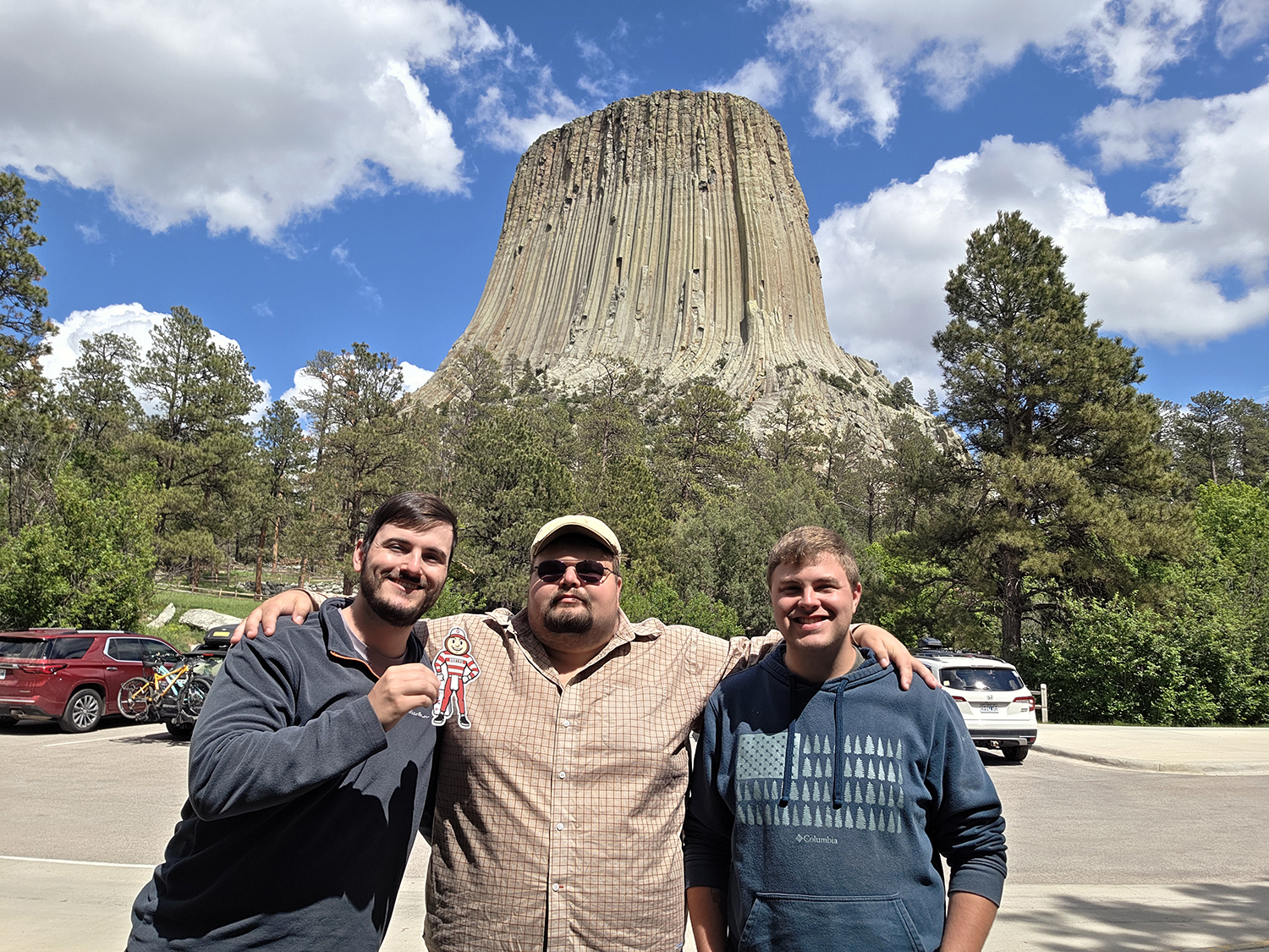 Three men, one holding Brutus, in front of Devil's Tower National Monument in Wyoming.