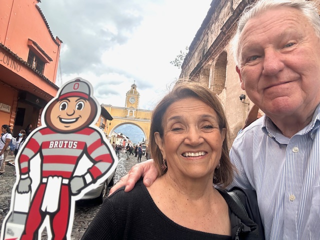 A man and woman with Brutus in the foreground of a pedestrian part of town in Antigua, Guatemala.