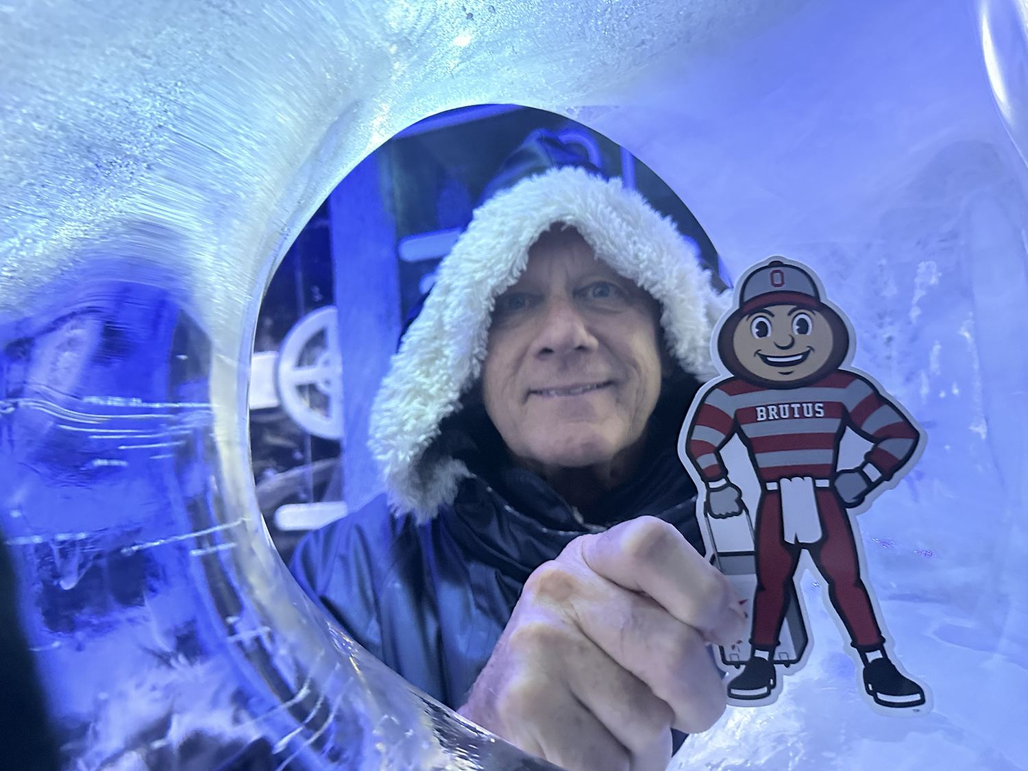 A man in a winter coat holding Brutus by an ice sculpture in Stockholm, Sweden.