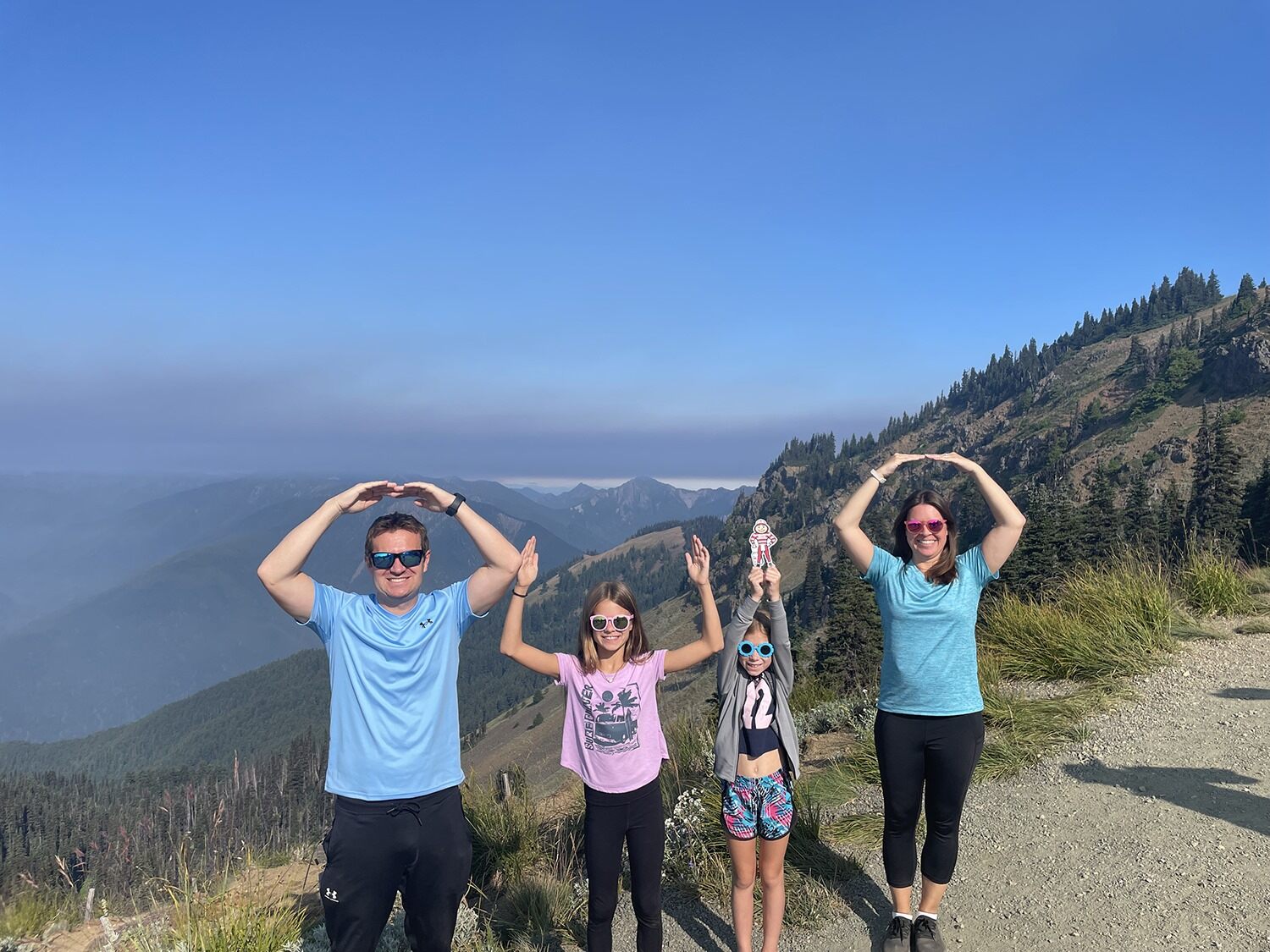Four people posing on a mountain trail with scenic valley views forming O-H-I-O with their arms.