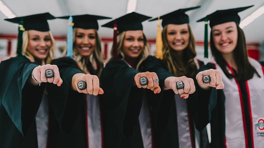 Five graduates in their cap and gown with their fists out showing their rings.
