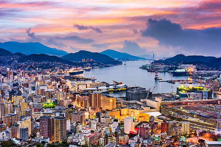 The Nagasaki coastal city and harbor surrounded by hills at sunset.