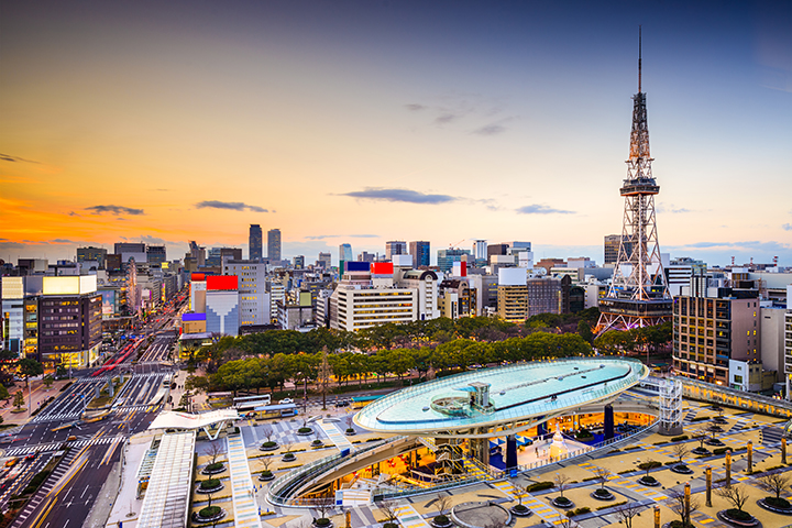 A modern Nagoya cityscape with a glass-roofed structure and a tall tower at sunset.