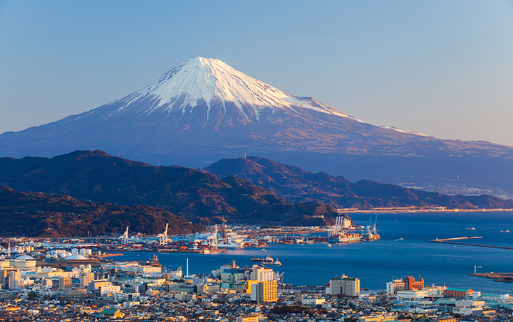 A coastal city sits along the water with snow‑capped Mount Fuji rising in the background.