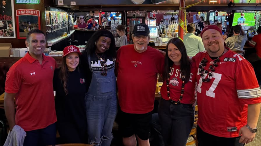 A group of people standing together inside a bar or restaurant, all wearing Ohio State–themed clothing and posing for a photo.