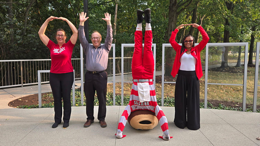 People standing outdoors forming the letters O‑H‑I‑O with Brutus Buckeye doing a handstand as the “I.”