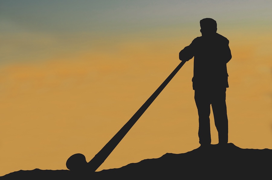 Alphorn musician standing outside with an orange sky in the background at sunset
