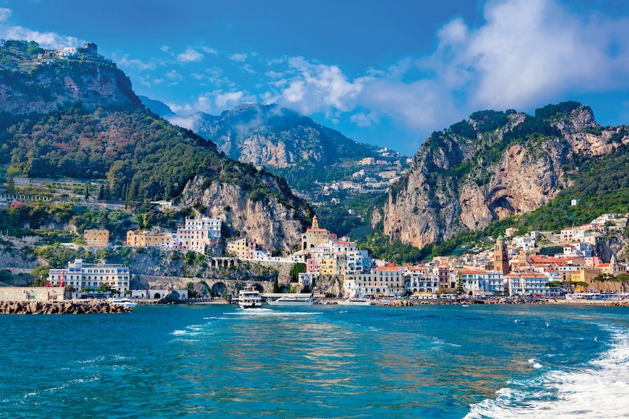Seafront view of Amalfi town along the Amalfi Coast, Italy, featuring colorful buildings cascading down toward the sparkling Mediterranean Sea.