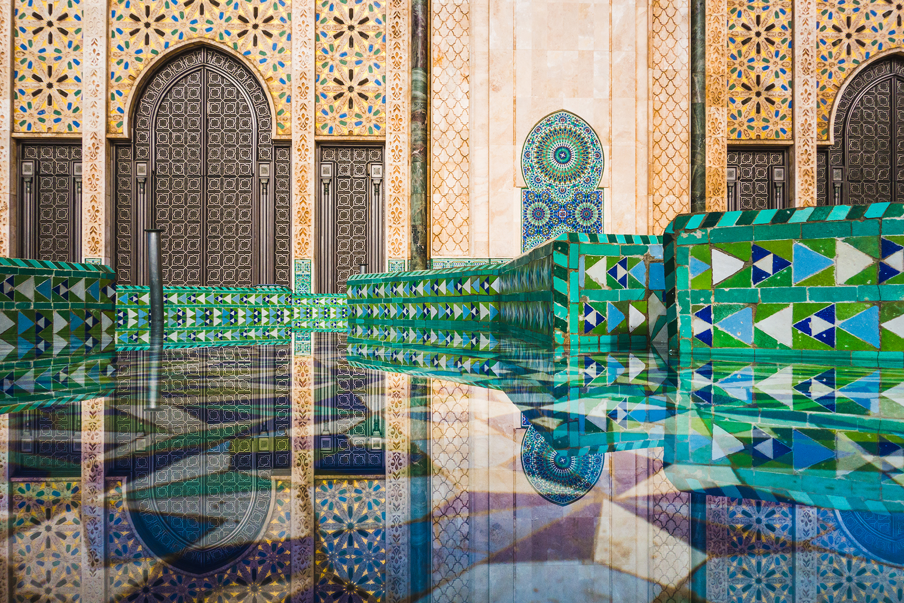 Ornate mosque facade with intricate geometric mosaic tiles in green, blue, and white, reflecting in a calm pool, conveying tranquility and harmony.